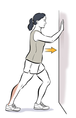 Woman leaning hands on wall doing calf stretch.