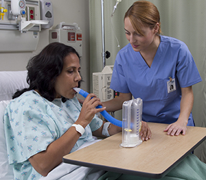 Healthcare provider showing woman in hospital bed how to use incentive spirometer.