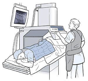 Woman lying face down on table under scanner. Health care provider wearing lead vest is tilting table and looking at monitor.